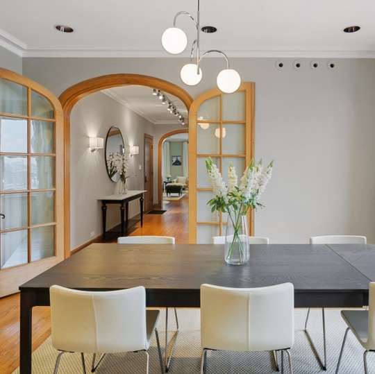 Dining area with a dark table and white chairs, opening through arched wood-framed doorways to a hallway.
